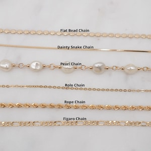 May include: A close-up of six different gold chains, including a flat bead chain, a dainty snake chain, a pearl chain, a rolo chain, a rope chain, and a figaro chain.