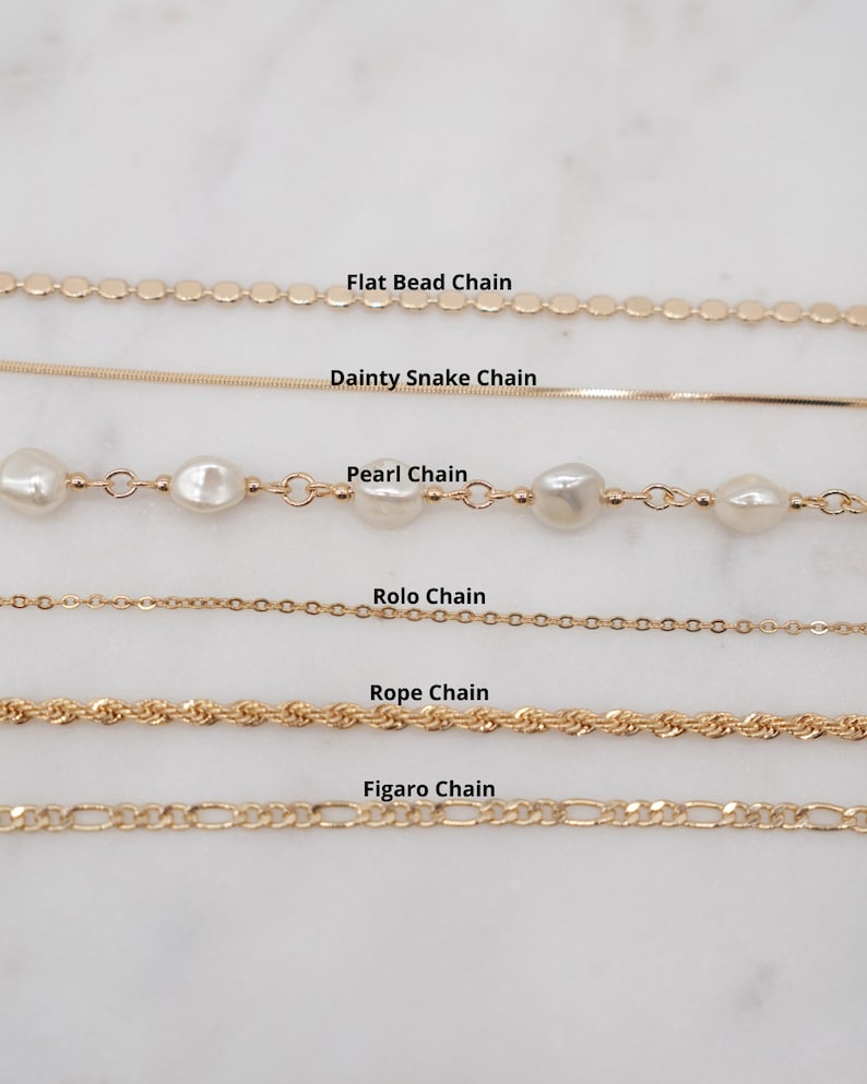 May include: A close-up of six different gold chains, including a flat bead chain, a dainty snake chain, a pearl chain, a rolo chain, a rope chain, and a figaro chain.