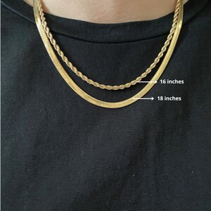 Pode incluir: Duas correntes de ouro, uma com 40,6 cm e outra com 45,7 cm de comprimento, s&atilde;o sobrepostas no pesco&ccedil;o de uma pessoa. Ambas as correntes s&atilde;o de ouro e t&ecirc;m um acabamento brilhante.