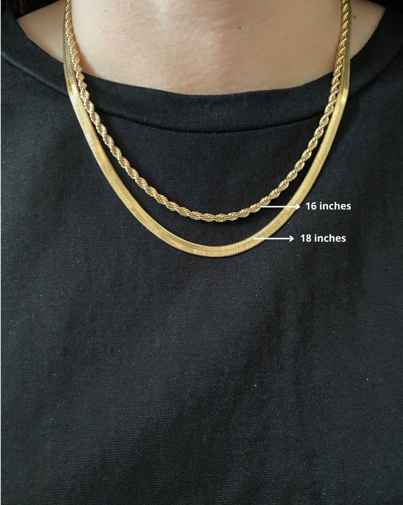 Pode incluir: Duas correntes de ouro, uma com 40,6 cm e outra com 45,7 cm de comprimento, s&atilde;o sobrepostas no pesco&ccedil;o de uma pessoa. Ambas as correntes s&atilde;o de ouro e t&ecirc;m um acabamento brilhante.