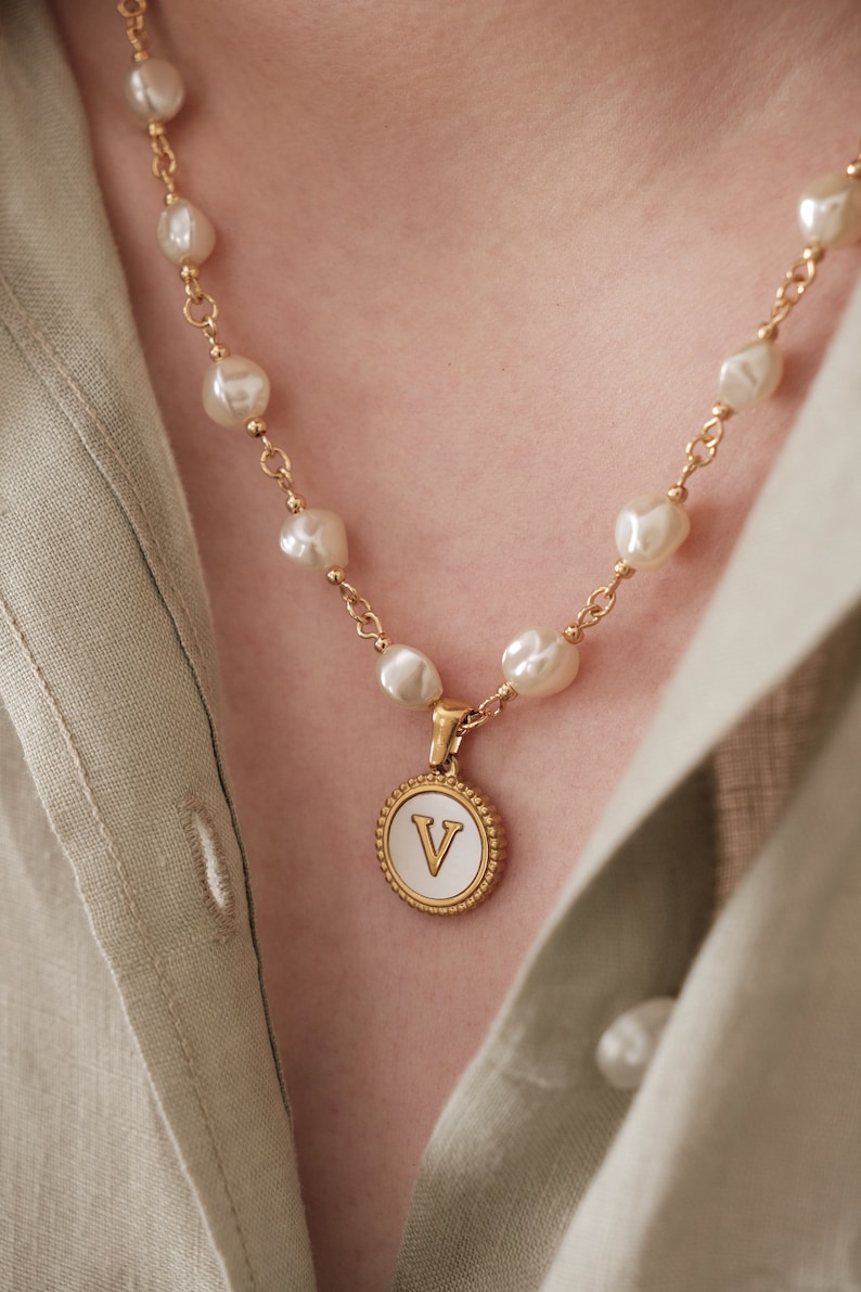 May include: A gold necklace with a white pearl chain and a gold pendant with a white enamel letter V.