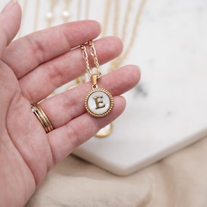May include: A gold chain necklace with a white mother-of-pearl pendant featuring the letter "E" in gold.
