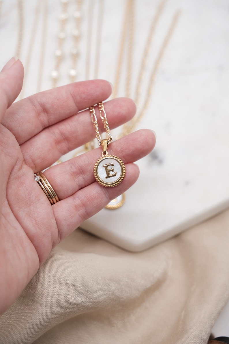 May include: A gold chain necklace with a white mother-of-pearl pendant featuring the letter "E" in gold.