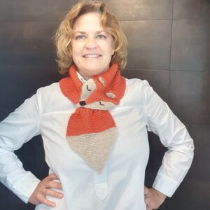 May include: A woman wearing a white button-down shirt with a knitted fox scarf. The scarf is orange and beige with a fox face design.