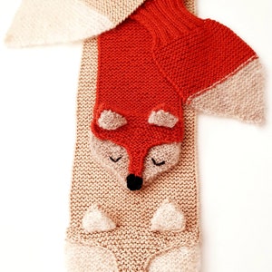 May include: A knitted scarf with two fox faces, one orange and one beige. The scarf is made with a soft, fluffy yarn.