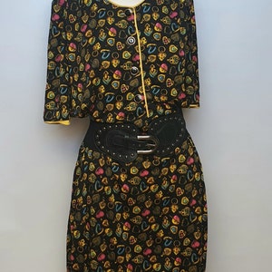 May include: A black dress with a yellow trim and a colourful print of hearts and keys. The dress has a black belt with silver studs.