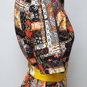 May include: A vintage short-sleeved shirt with a patchwork design featuring geometric shapes and floral patterns in shades of orange, red, yellow, white, and black. The shirt has a yellow belt.