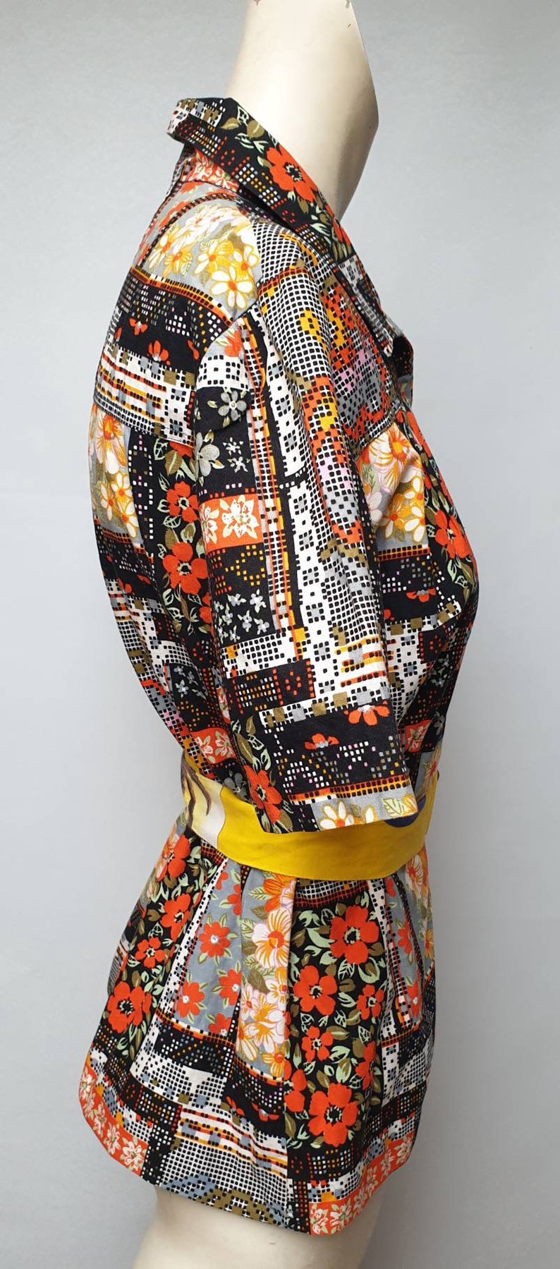 May include: A vintage short-sleeved shirt with a patchwork design featuring geometric shapes and floral patterns in shades of orange, red, yellow, white, and black. The shirt has a yellow belt.