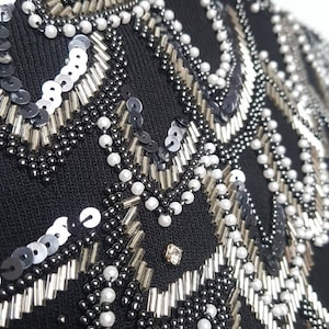 May include: Black knit fabric with a detailed design of silver and black beads and sequins. The design is a repeating pattern of curved lines and circles.