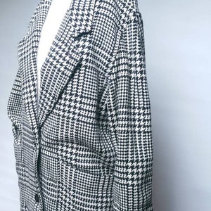 May include: A black and white houndstooth blazer with a single button closure and two pockets. The blazer has a relaxed fit and is made of a soft, textured fabric.