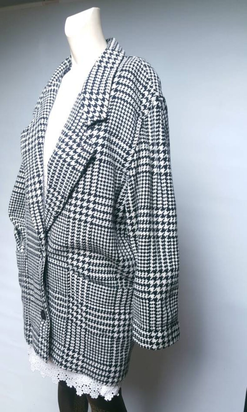 May include: A black and white houndstooth blazer with a single button closure and two pockets. The blazer has a relaxed fit and is made of a soft, textured fabric.