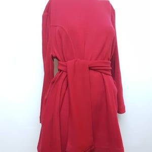 May include: A red dress with long sleeves and a sash that ties at the waist. The sash has a fringe detail.