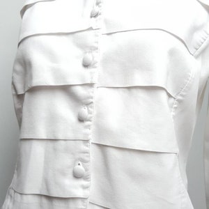 May include: White button-up blouse with a ruffled front and long sleeves.