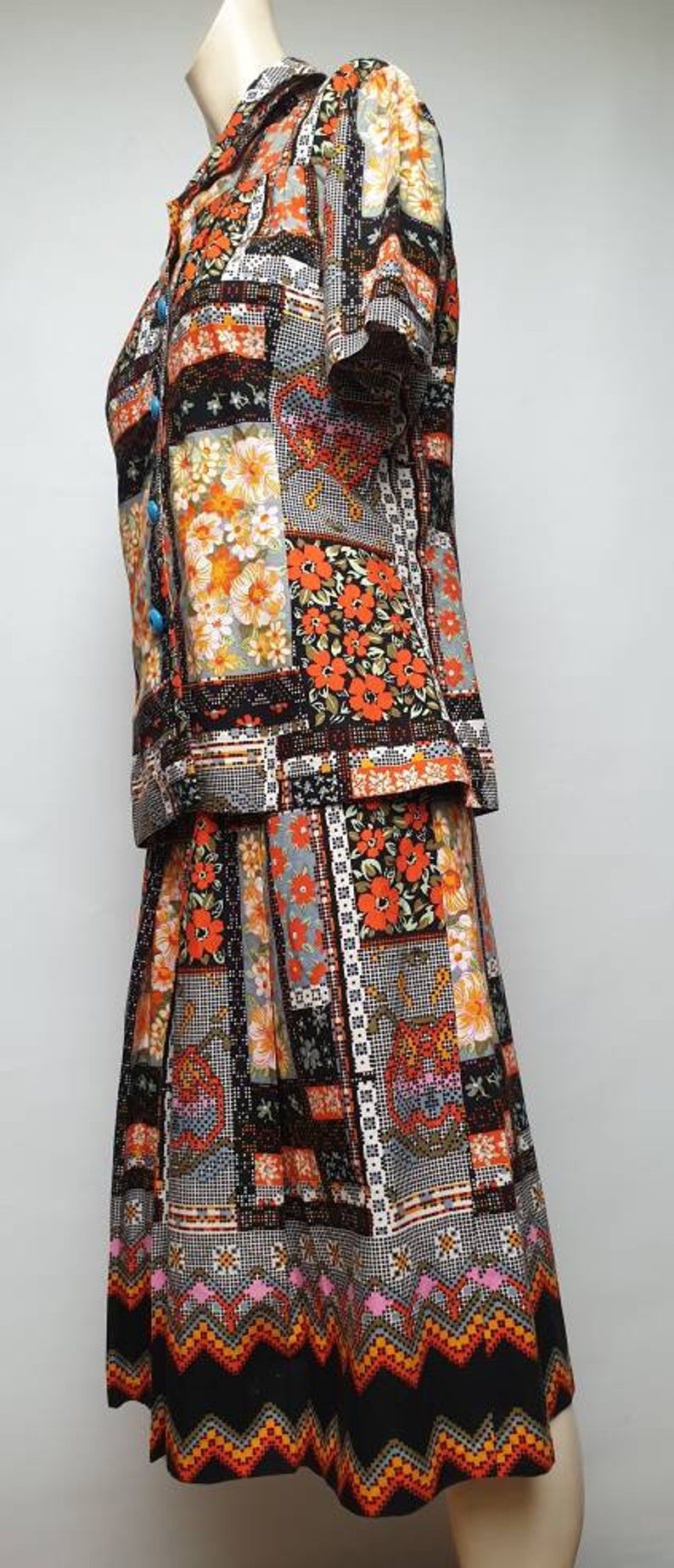 May include: A vintage-style dress with a patchwork design featuring orange, black and white floral patterns. The dress has a short-sleeved top and a skirt with a scalloped hem.
