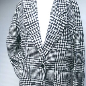 May include: A black and white houndstooth patterned blazer with a single button closure. The blazer has a collar and two pockets.
