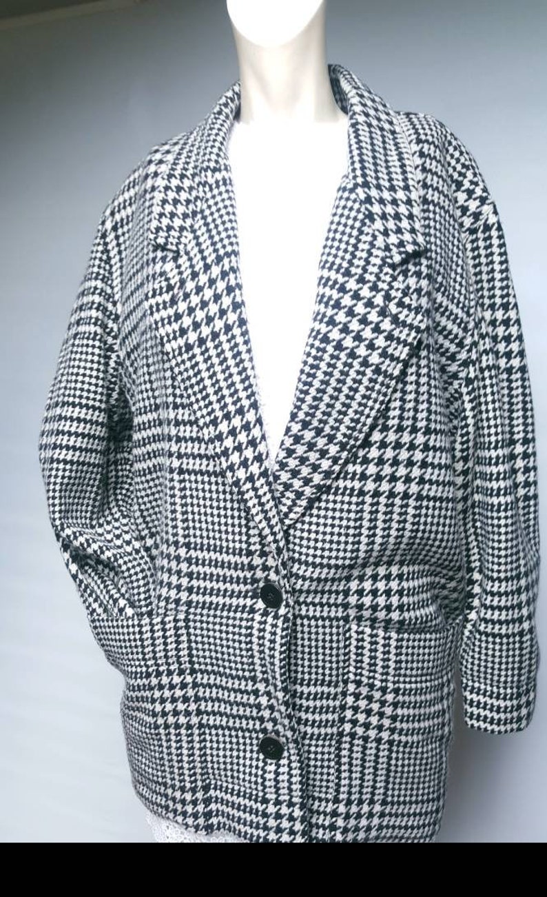 May include: A black and white houndstooth patterned blazer with a single button closure. The blazer has a collar and two pockets.