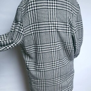 May include: Black and white houndstooth patterned coat with a long sleeve and a collar.