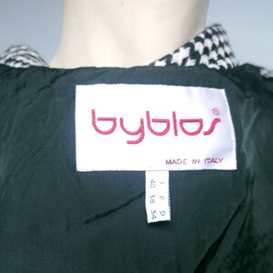 May include: A black and white houndstooth jacket with a black lining. The label reads "Byblos" in red lettering and "Made in Italy". The size tag reads "I F D 40 38 34".