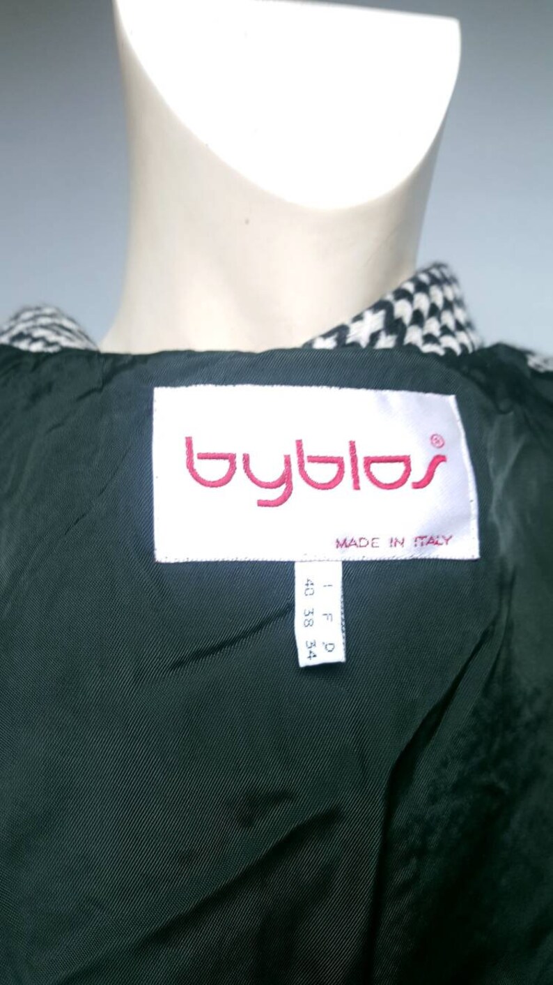 May include: A black and white houndstooth jacket with a black lining. The label reads "Byblos" in red lettering and "Made in Italy". The size tag reads "I F D 40 38 34".