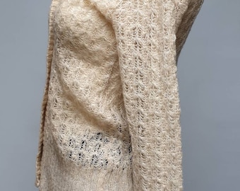 May include: A beige knitted cardigan with a delicate openwork pattern. The cardigan has long sleeves and a v-neck.