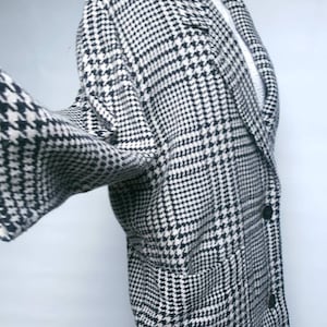 May include: A black and white houndstooth patterned coat with a long sleeve and a double breasted closure.