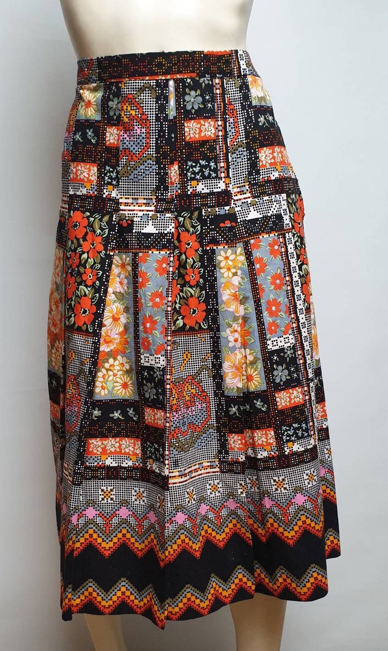May include: A black midi skirt with a colourful patchwork design featuring orange, red and white flowers. The skirt has a geometric pattern at the hem.