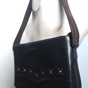 Könnte beinhalten: Eine schwarze Lederschultertasche mit braunem Riemen und einem ausgeschnittenen Design. Die Tasche hat das Wort "Barneys" auf der Vorderseite geprägt.