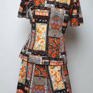 May include: A two-piece outfit consisting of a short-sleeved blouse and a skirt. Both pieces feature a patchwork design with orange, black and white floral patterns.