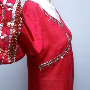 Peut inclure: Une tunique rouge à manches longues avec des paillettes et des perles argentées et cuivrées. Les paillettes sont disposées en motif sur les manches et l'encolure.