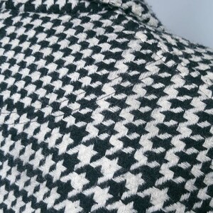 May include: Close-up of a black and white houndstooth patterned fabric. The fabric is woven with a subtle texture.