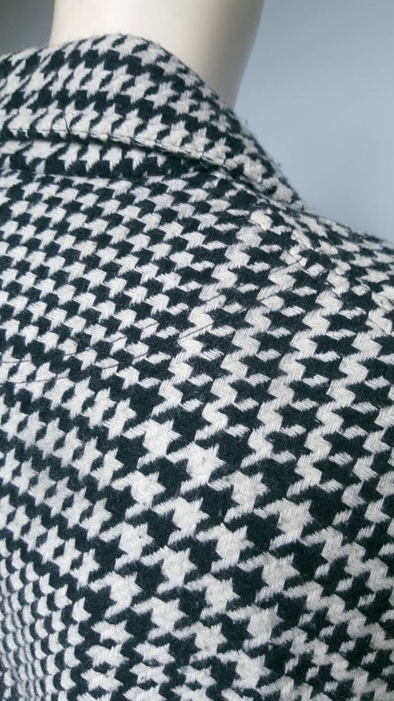 May include: Close-up of a black and white houndstooth patterned fabric. The fabric is woven with a subtle texture.
