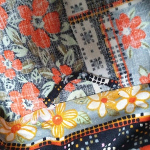 May include: Close-up of a multi-coloured fabric with a floral pattern. The fabric features a variety of colours, including orange, black, white, and yellow. The fabric is made of a soft, comfortable material and has a textured surface.