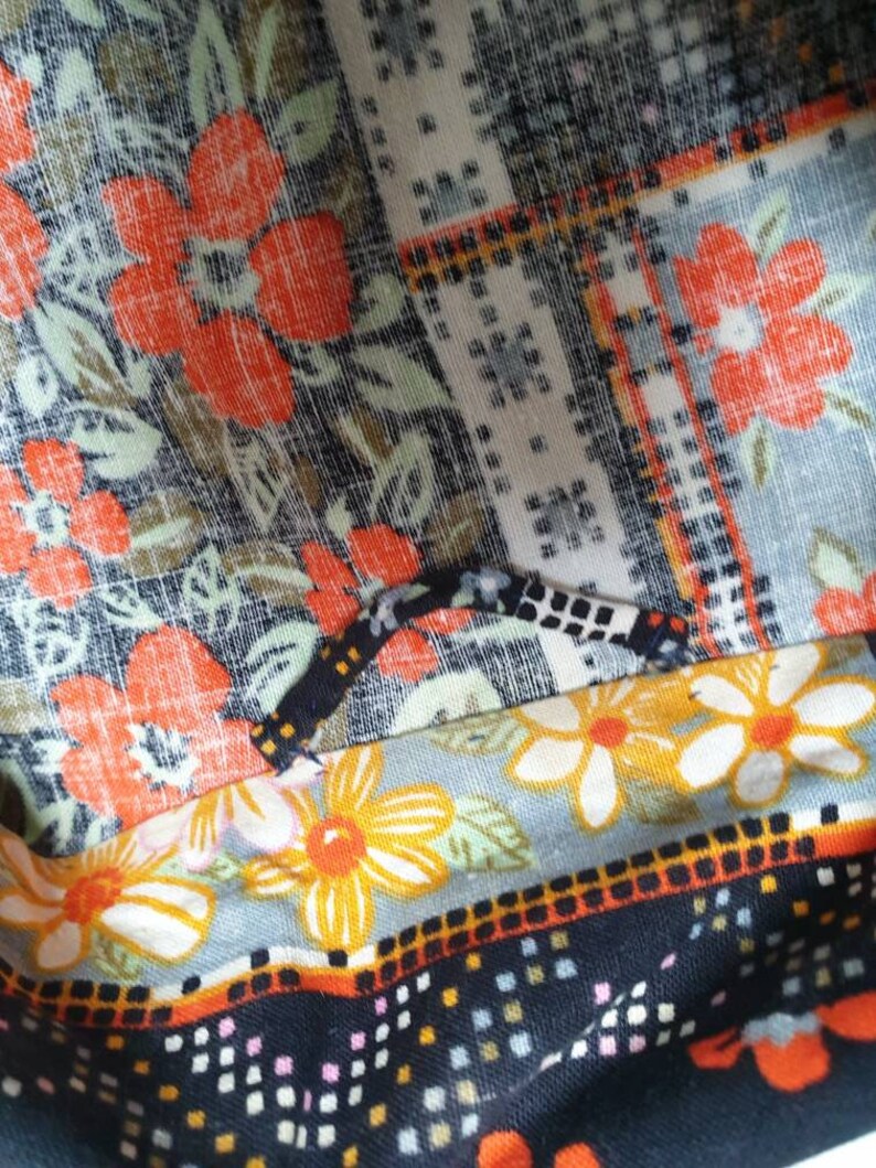 May include: Close-up of a multi-coloured fabric with a floral pattern. The fabric features a variety of colours, including orange, black, white, and yellow. The fabric is made of a soft, comfortable material and has a textured surface.