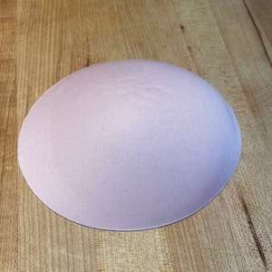 Puede incluir: Un círculo de tela rosa claro, posiblemente una almohadilla de sujetador o un proyecto de costura, sobre una superficie de madera.