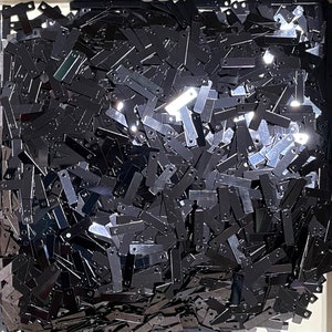 May include: A large pile of black metal sequins, all in the shape of a rectangle with a small hole at each end. The sequins are scattered randomly and appear to be made of a shiny, reflective material.