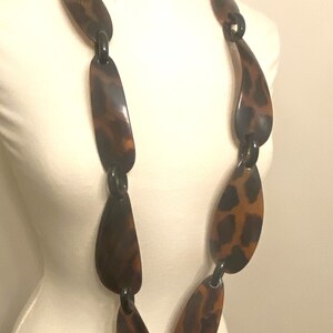 Peut inclure: Un long collier brun et noir compos&eacute; de maillons en plastique de forme ovale. Les maillons ont un motif l&eacute;opard.