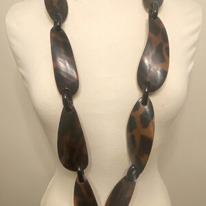 Peut inclure: Un long collier brun et noir compos&eacute; de grandes pi&egrave;ces ovales. Les pi&egrave;ces sont reli&eacute;es par des anneaux noirs.