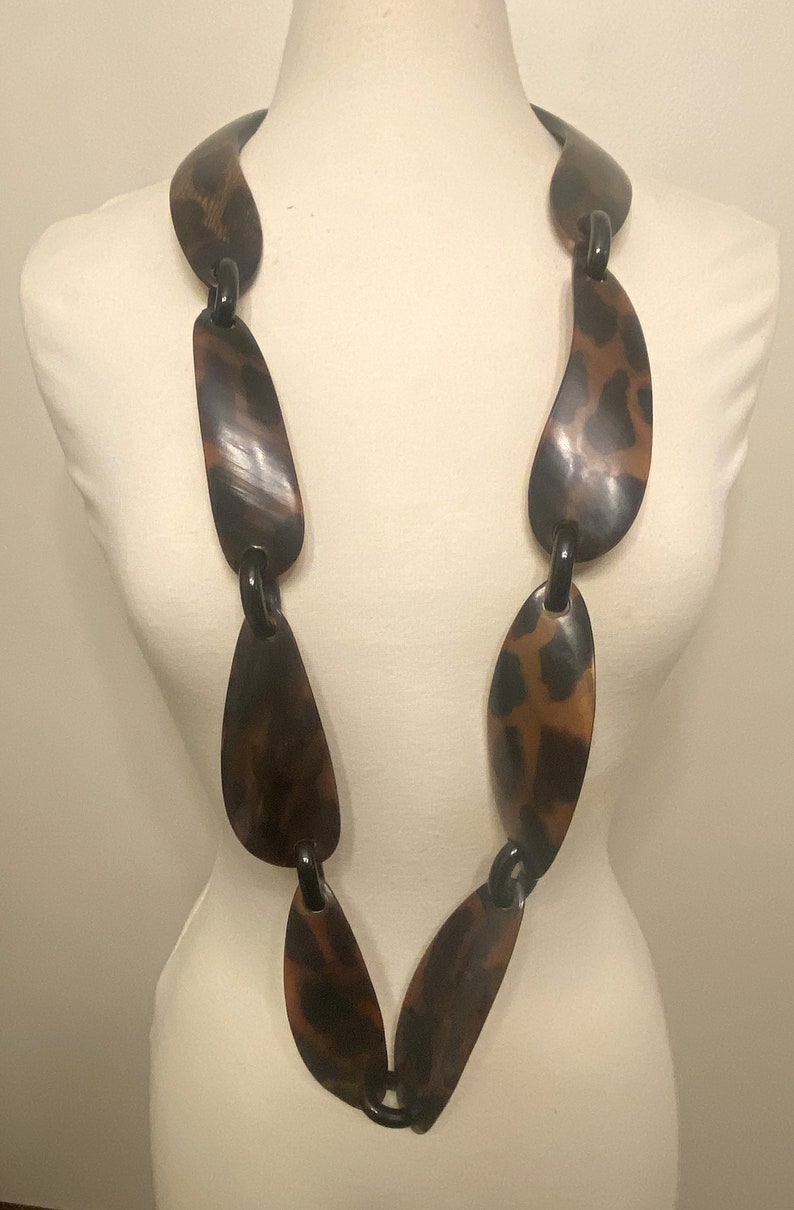 Peut inclure: Un long collier brun et noir compos&eacute; de grandes pi&egrave;ces ovales. Les pi&egrave;ces sont reli&eacute;es par des anneaux noirs.