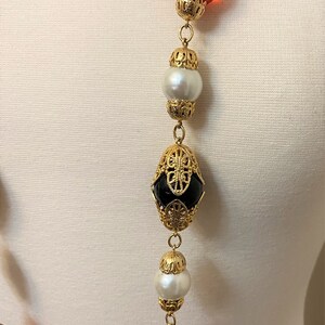 May include: A gold chain necklace with alternating amber, black, and white beads. The beads are set in ornate gold frames.