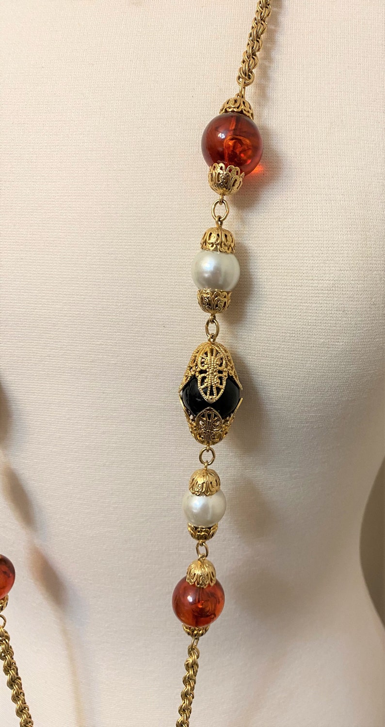 May include: A gold chain necklace with alternating amber, black, and white beads. The beads are set in ornate gold frames.