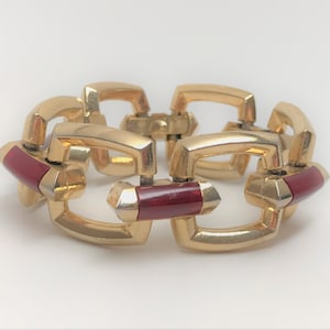 May include: Gold tone bracelet with a chain link design. Each link has a red enamel inlay.