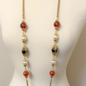 May include: A gold chain necklace with alternating amber, white pearl, and black and gold beads.
