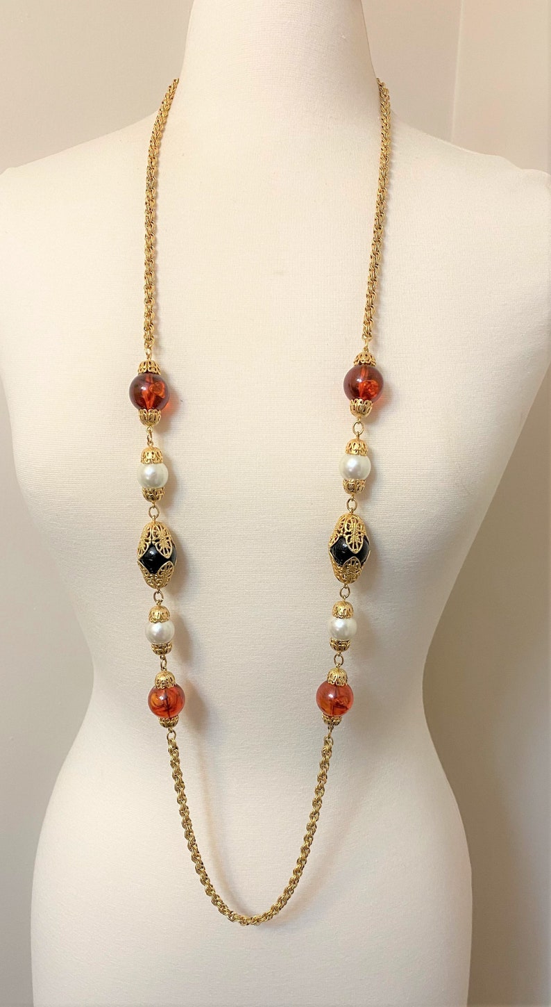 May include: A gold chain necklace with alternating amber, white pearl, and black and gold beads.