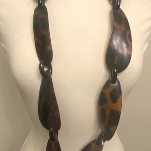 Peut inclure: Un long collier brun et noir compos&eacute; de gros maillons ovales &agrave; motif l&eacute;opard.