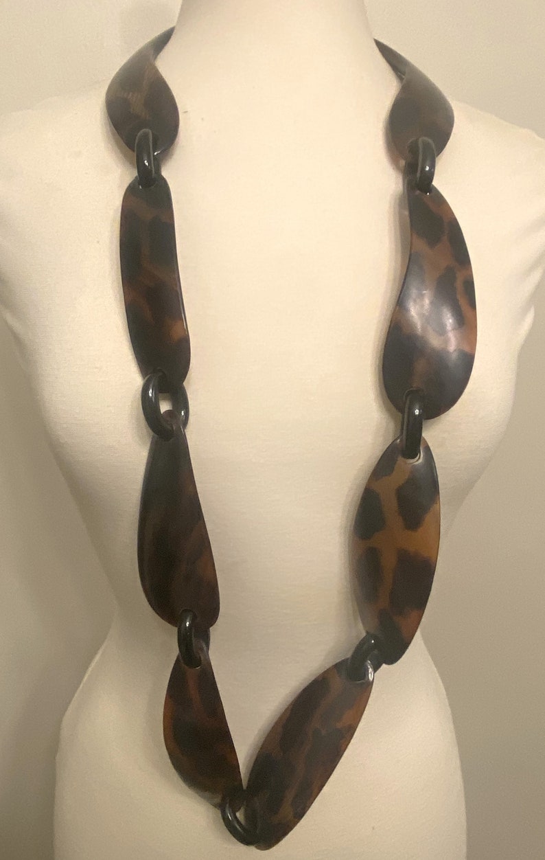 Peut inclure: Un long collier brun et noir compos&eacute; de gros maillons ovales &agrave; motif l&eacute;opard.