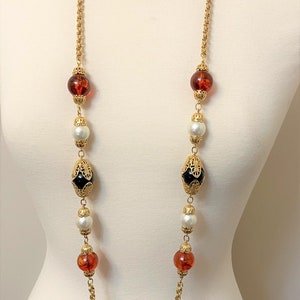 May include: A long gold chain necklace with alternating amber, white pearl, and black and gold beads.
