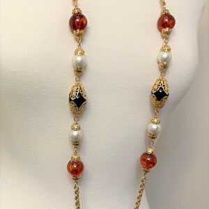 May include: A long gold chain necklace with alternating amber, white pearl, and black beads with gold filigree accents.