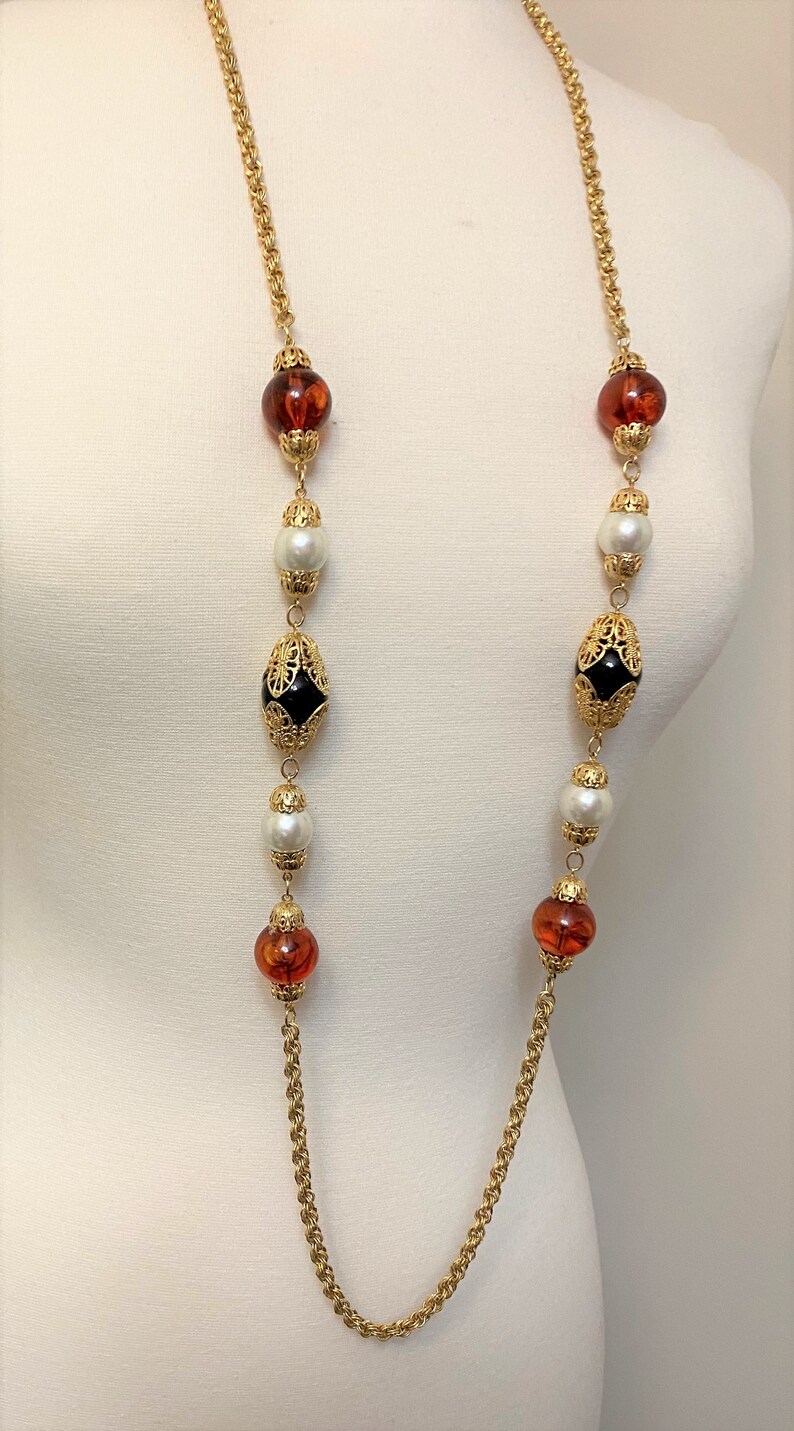May include: A long gold chain necklace with alternating amber, white pearl, and black beads with gold filigree accents.