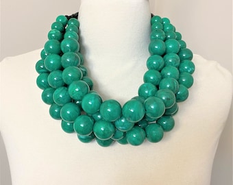May include: A chunky statement necklace made of large, green, marbled beads. The necklace is layered and has a thick, rounded shape.