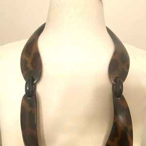 Peut inclure: Un long collier en plastique brun et noir avec un motif l&eacute;opard. Le collier est compos&eacute; de plusieurs pi&egrave;ces reli&eacute;es.